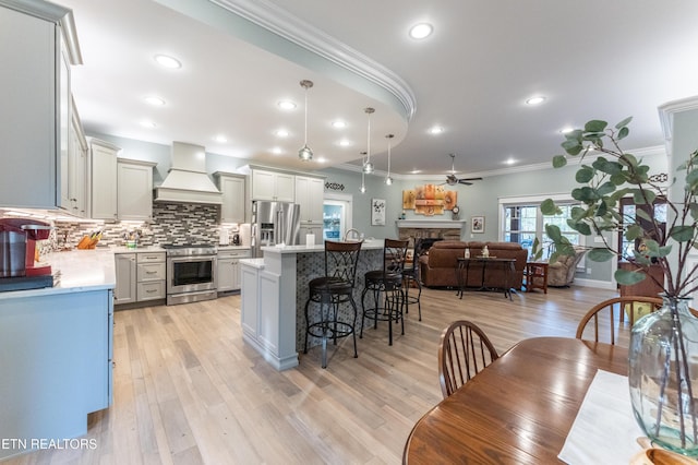 kitchen with custom exhaust hood, stainless steel appliances, light countertops, a kitchen island, and a stone fireplace