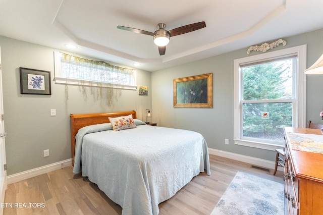 bedroom featuring light wood finished floors, baseboards, visible vents, a raised ceiling, and a ceiling fan