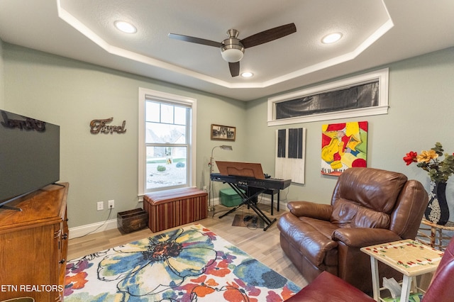 sitting room with baseboards, a raised ceiling, a ceiling fan, and light wood-style floors