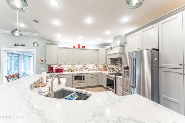 kitchen with premium appliances, custom range hood, light stone counters, decorative light fixtures, and a sink