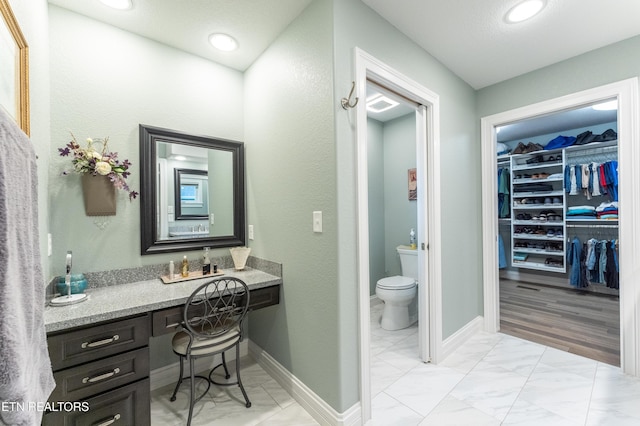 bathroom featuring marble finish floor, a walk in closet, toilet, and baseboards