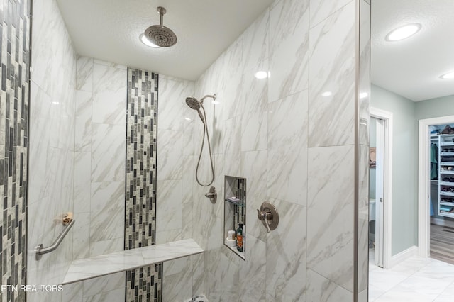 bathroom with a textured ceiling, marble finish floor, a tile shower, and a walk in closet