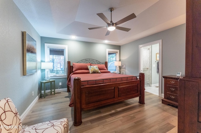 bedroom with a tray ceiling, light wood finished floors, multiple windows, and connected bathroom