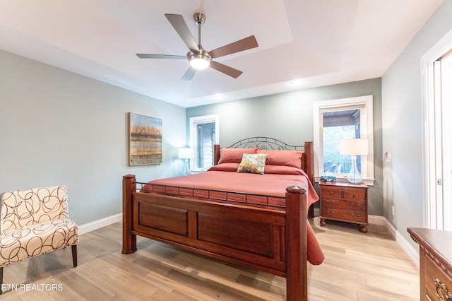 bedroom with a ceiling fan, a raised ceiling, light wood-style flooring, and baseboards