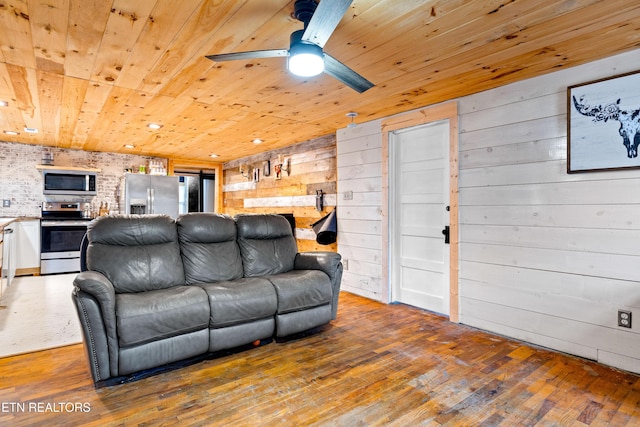 living area featuring ceiling fan, wooden ceiling, wood finished floors, and wooden walls