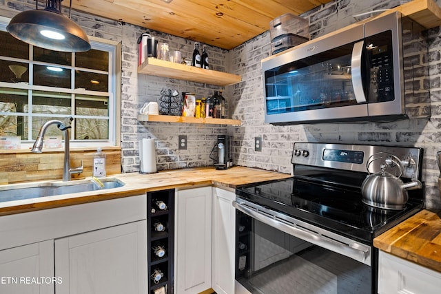 kitchen featuring pendant lighting, wooden counters, appliances with stainless steel finishes, white cabinets, and a sink