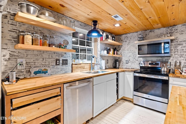 kitchen featuring white cabinets, wooden counters, appliances with stainless steel finishes, open shelves, and pendant lighting