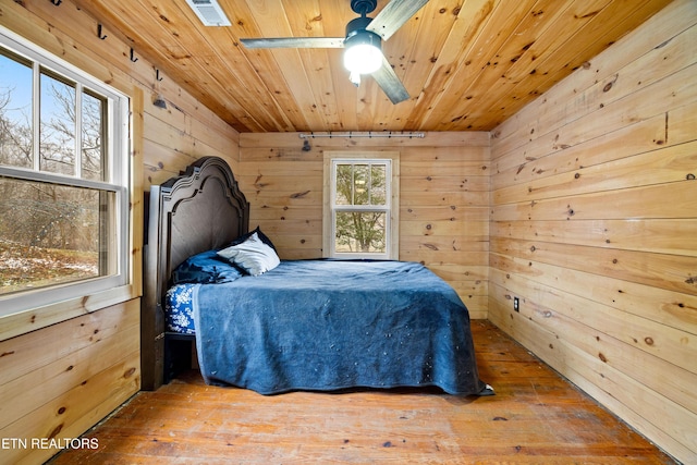 bedroom with visible vents, wood ceiling, ceiling fan, wooden walls, and wood finished floors