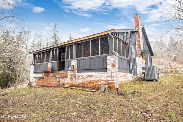 view of front facade featuring a sunroom, a chimney, and central AC