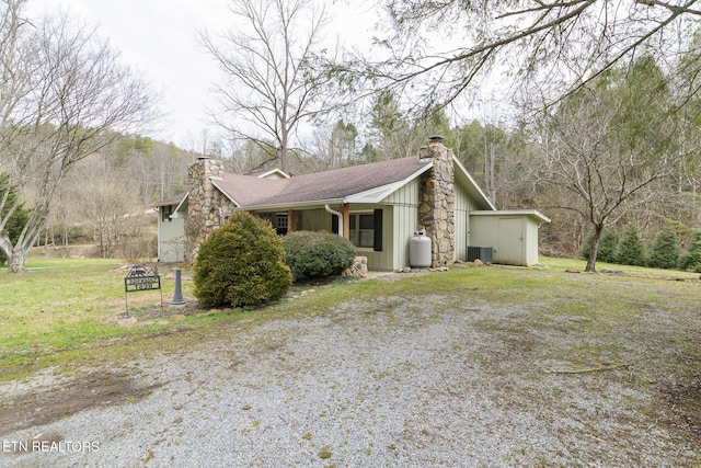 view of side of property with a yard, a chimney, board and batten siding, cooling unit, and driveway