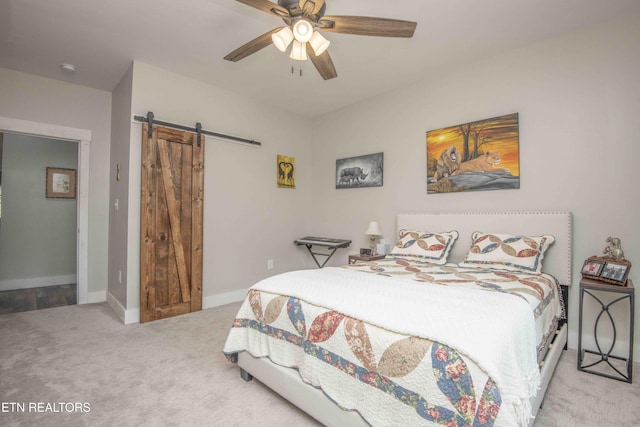 bedroom with light carpet, ceiling fan, a barn door, and baseboards