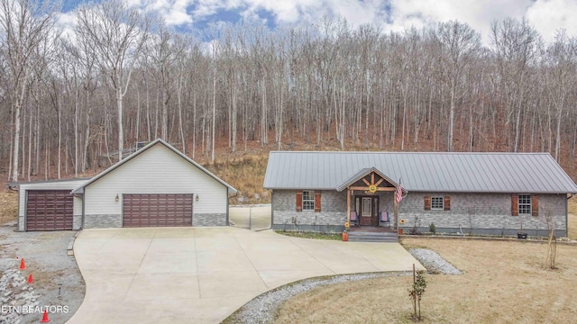 view of front of property with a forest view, stone siding, a detached garage, and metal roof