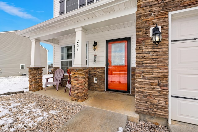 snow covered property entrance with a porch and stone siding