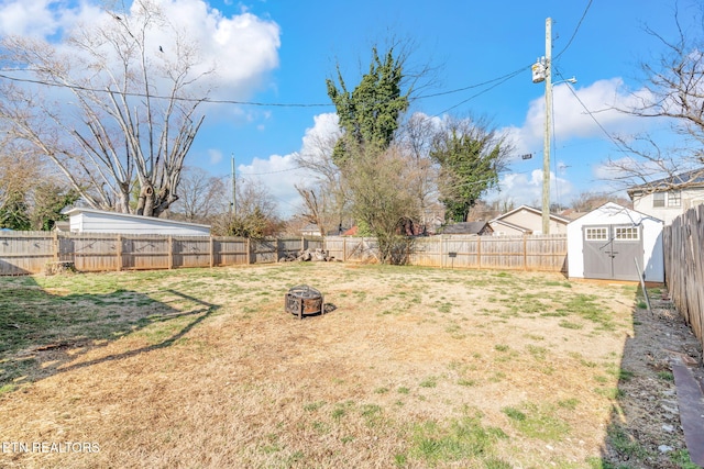 view of yard with a fire pit, a storage shed, an outdoor structure, and a fenced backyard