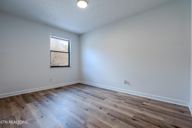 unfurnished room with visible vents, a textured ceiling, baseboards, and wood finished floors