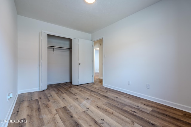 unfurnished bedroom featuring light wood-style flooring, baseboards, and a closet