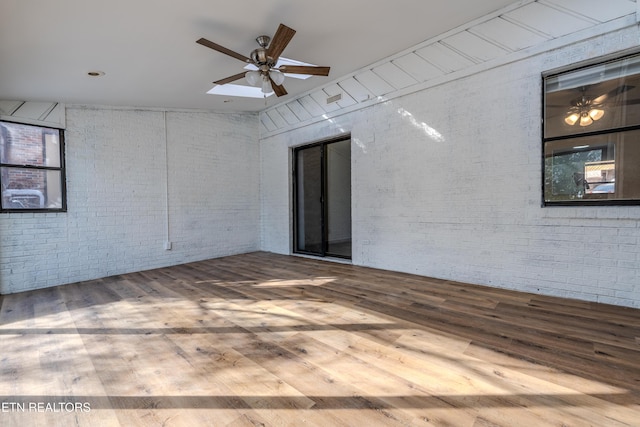 empty room with light wood-style floors, brick wall, and ceiling fan