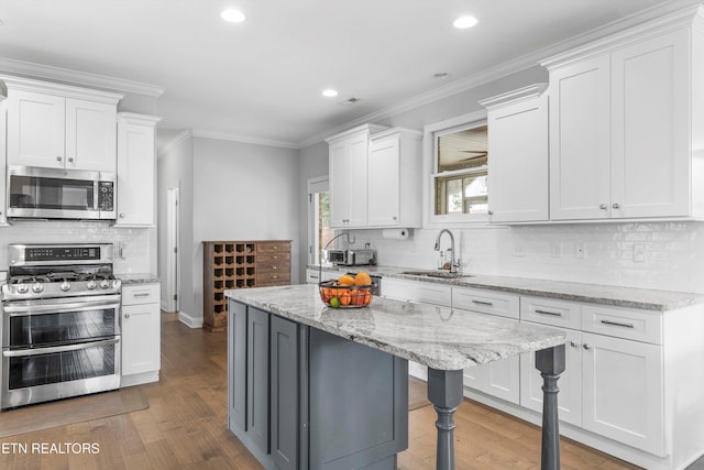 kitchen featuring appliances with stainless steel finishes, white cabinetry, a kitchen island, a sink, and light stone countertops