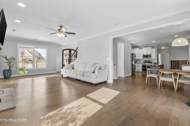 living room with ceiling fan, ornamental molding, dark wood-style flooring, and baseboards