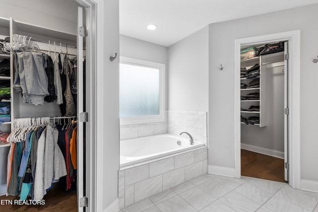 bathroom featuring a garden tub, a spacious closet, and baseboards