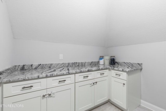 kitchen featuring light stone counters, white cabinets, vaulted ceiling, and a textured ceiling