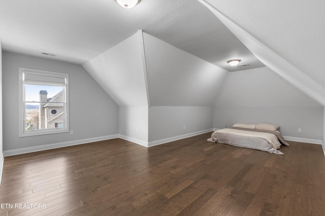 unfurnished bedroom featuring a textured ceiling, visible vents, baseboards, vaulted ceiling, and dark wood finished floors