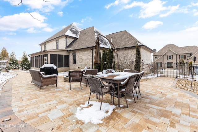 snow covered patio featuring a sunroom, a grill, fence, and outdoor dining area