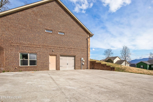 view of side of property with concrete driveway, brick siding, and an attached garage