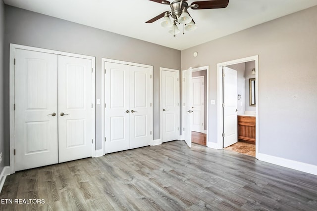 unfurnished bedroom featuring baseboards, a ceiling fan, connected bathroom, wood finished floors, and two closets