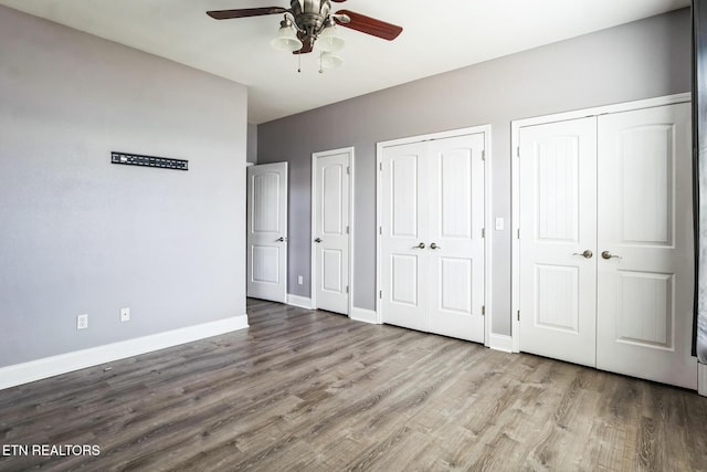 unfurnished bedroom featuring ceiling fan, wood finished floors, two closets, and baseboards