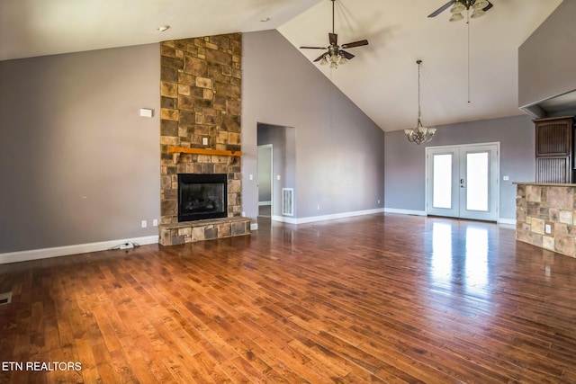 unfurnished living room with hardwood / wood-style flooring, baseboards, ceiling fan with notable chandelier, and a stone fireplace