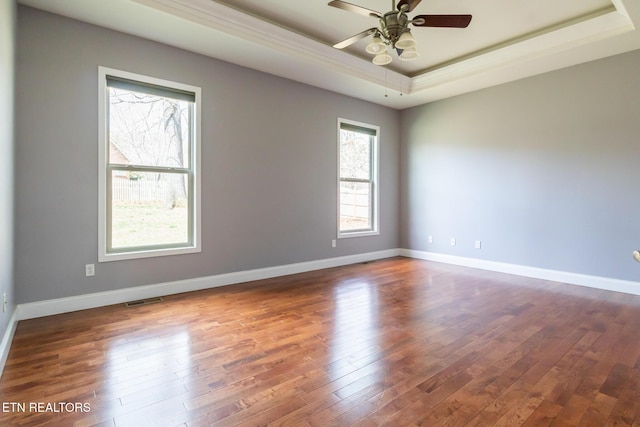 spare room featuring dark wood-style floors, a tray ceiling, visible vents, ceiling fan, and baseboards