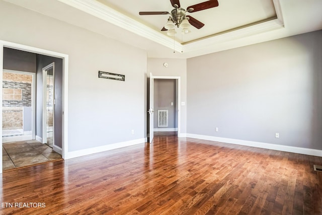 spare room featuring ceiling fan, wood finished floors, visible vents, baseboards, and a tray ceiling