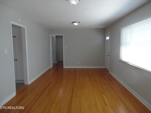 unfurnished room with light wood-style flooring, baseboards, and a textured ceiling