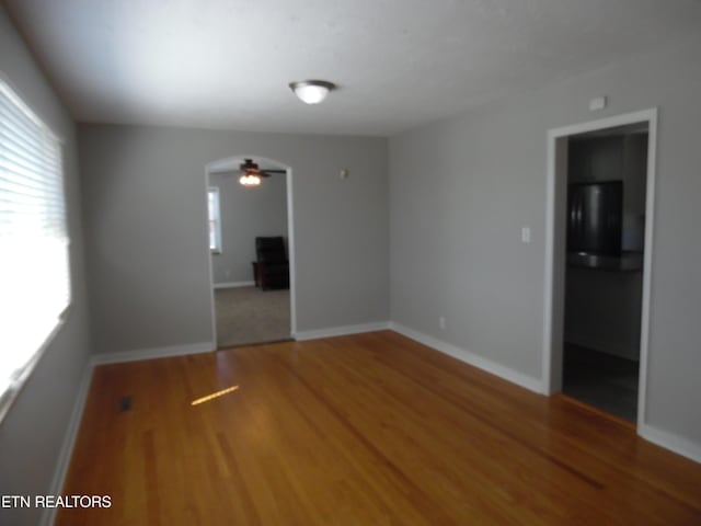 spare room featuring arched walkways, ceiling fan, baseboards, and wood finished floors