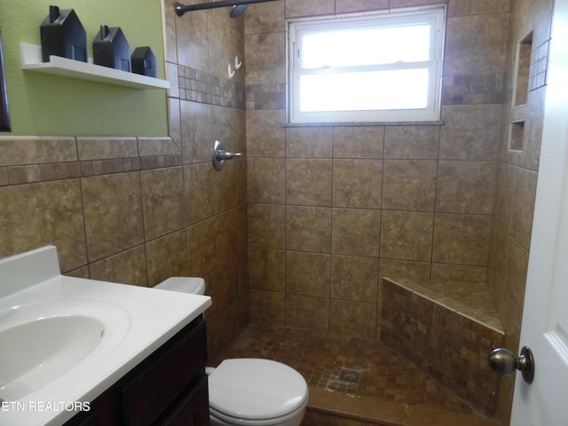 full bathroom featuring toilet, a tile shower, and vanity