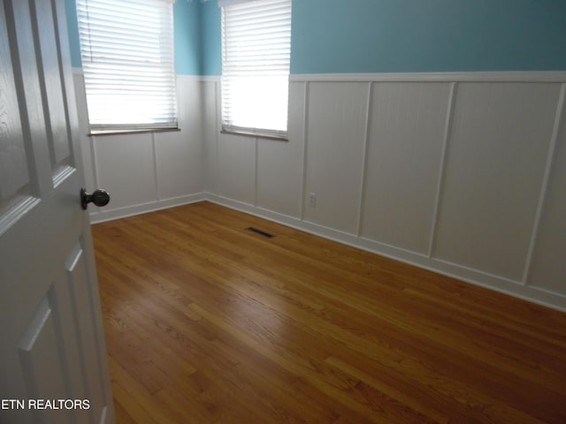 spare room with a wainscoted wall, visible vents, a decorative wall, and wood finished floors