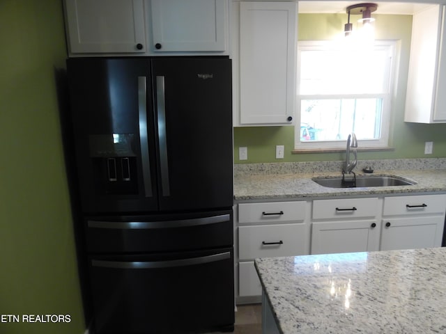 kitchen featuring a sink, light stone countertops, white cabinetry, and black fridge