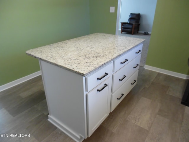 kitchen with light stone countertops, baseboards, open floor plan, white cabinets, and a center island