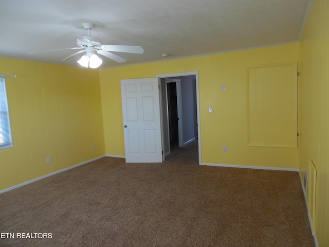 spare room featuring baseboards, dark carpet, a ceiling fan, and crown molding