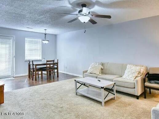 living area with a ceiling fan, a textured ceiling, baseboards, and wood finished floors