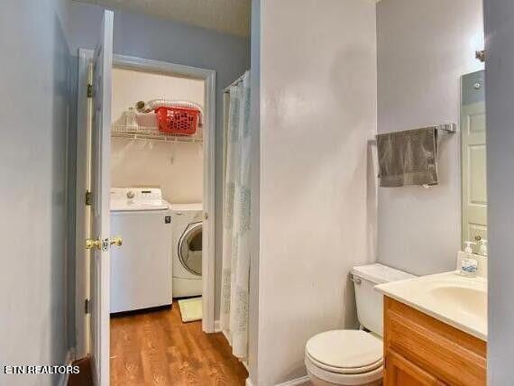 full bathroom featuring toilet, vanity, wood finished floors, and washing machine and clothes dryer