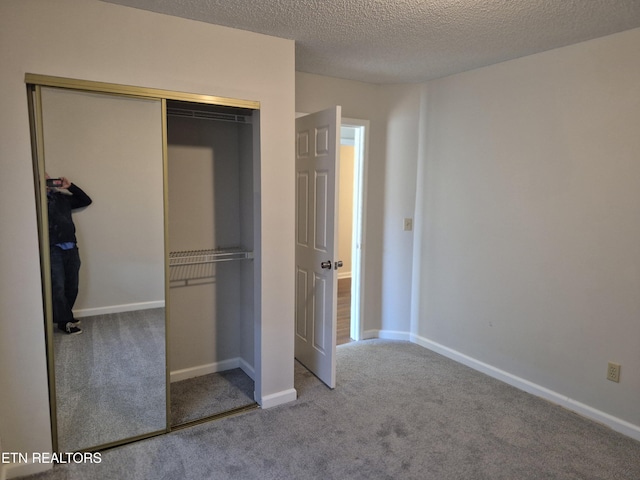 unfurnished bedroom with carpet floors, a closet, a textured ceiling, and baseboards