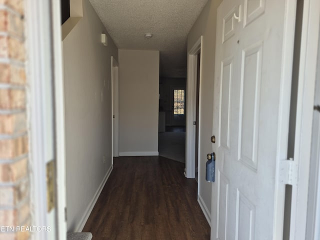 hall featuring dark wood finished floors, a textured ceiling, and baseboards