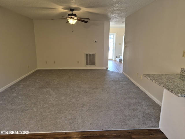 unfurnished living room with dark colored carpet, visible vents, a ceiling fan, a textured ceiling, and baseboards