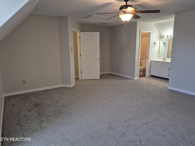 unfurnished bedroom featuring lofted ceiling, ensuite bathroom, carpet flooring, a textured ceiling, and baseboards