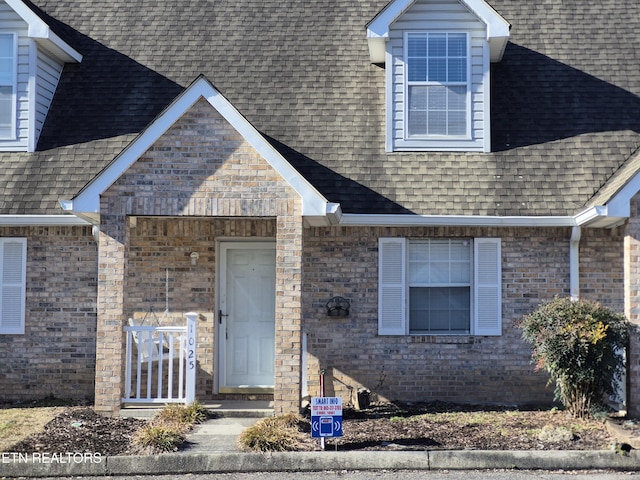 view of exterior entry with a shingled roof and brick siding