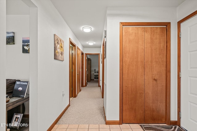 hallway with light carpet, baseboards, and light tile patterned floors