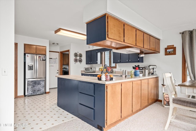 kitchen with stainless steel fridge, baseboards, brown cabinetry, light countertops, and light floors