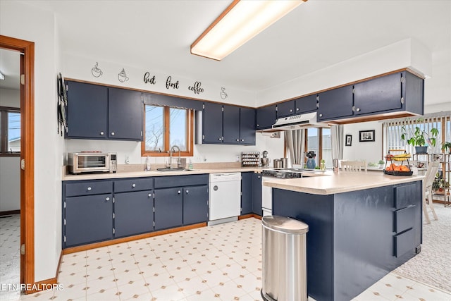 kitchen with light countertops, white dishwasher, a sink, a peninsula, and under cabinet range hood